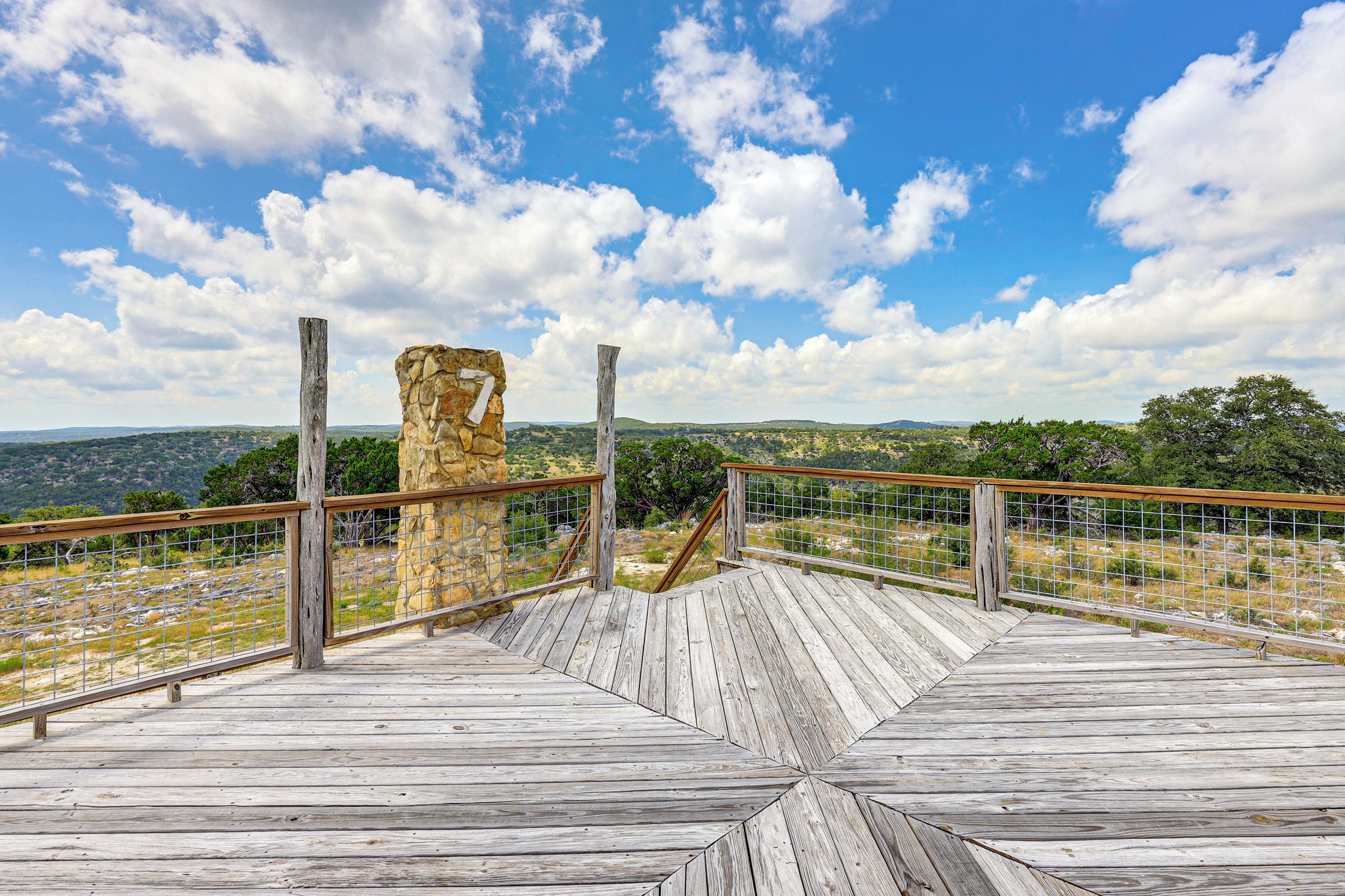 A wooden observation deck with a stone structure in the background, overlooking a hilly landscape.