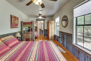 A room with a large bed, a ceiling fan, a window with a view, and a door leading to another room. - Horse Friendly! Hill Country Retreat w/ Views (Tarpley)