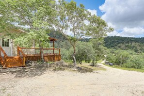 A wooden cabin with a porch, a dirt path, and a view of a hilly landscape.