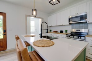 A modern kitchen with white cabinets, a stainless steel stove, and a large island with woven placemats. - Close to Dtwn & Med Center: Knoxville Home Base (Knoxville)