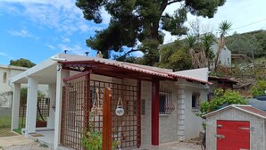 Una pequeña casa con puerta roja, patio cercado y jardín.