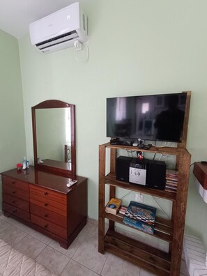 Una habitación con un aparador de madera, un espejo, un televisor sobre un mueble de madera y un equipo de aire acondicionado.