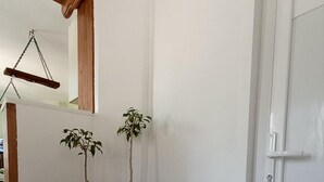 Una esquina con dos plantas en macetas sobre una pared blanca, una viga de madera y una puerta blanca.