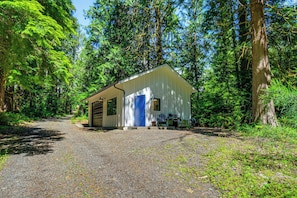 A small, single-story building with a blue door, surrounded by dense forest.