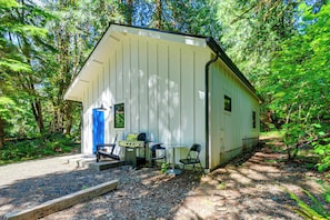 Une petite cabane avec une véranda, un barbecue et deux chaises.