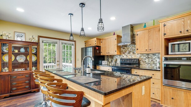 A kitchen with wooden cabinets, a central island, bar stools, and modern appliances. - 10-acre Retreat w/ Hiking! Gateway to Holden Beach (Shallotte)