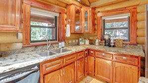 A wooden cabin interior with a kitchen featuring granite countertops, wooden cabinets, a dishwasher, and a refrigerator. - Forest, Fairways, Lake Almanor Days! Lake Love (Westwood)