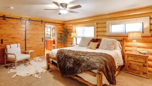 A log cabin bedroom with a bed, a chair, a nightstand, a ceiling fan, and a window. - Forest, Fairways, Lake Almanor Days! Lake Love (Westwood)