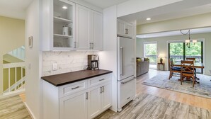 Una cocina moderna con armarios blancos, horno empotrado y comedor con mesa y sillas de madera.