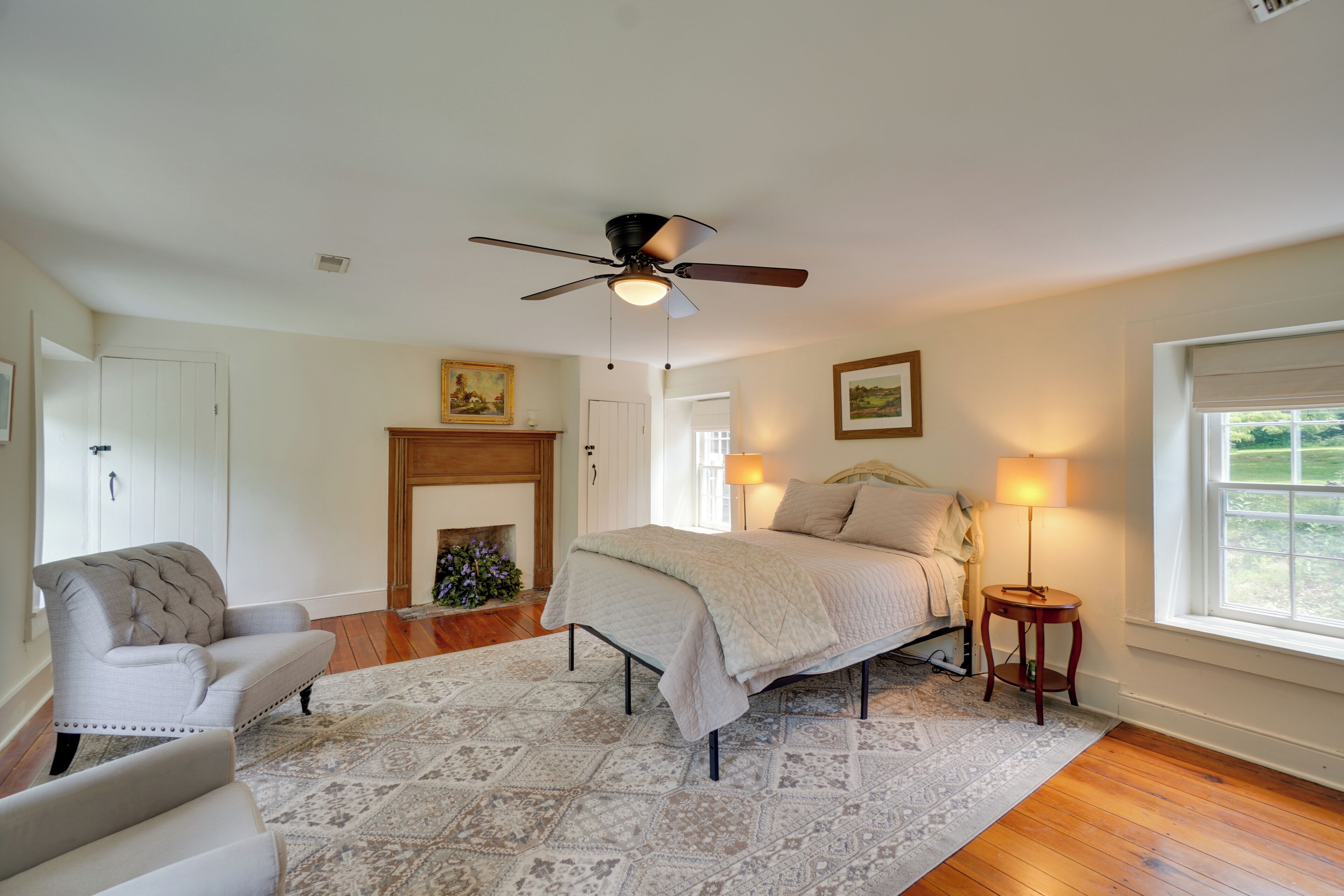 A bedroom with a bed, a chair, a fireplace, a ceiling fan, and a window.