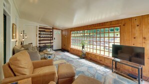 A living room with a stone floor, wooden paneled walls, a large window, and a television.