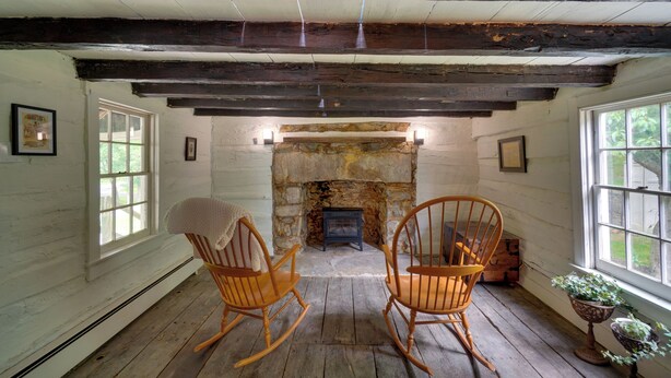 A room with wooden floors, a stone fireplace, two rocking chairs, and a window with a view.