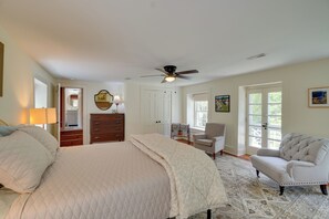 A bedroom with a bed, a chair, a desk, a ceiling fan, and a door.