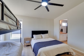 Quarto com cama beliche, uma cama de solteiro, ventoinha no teto, mesa de cabeceira e janela.