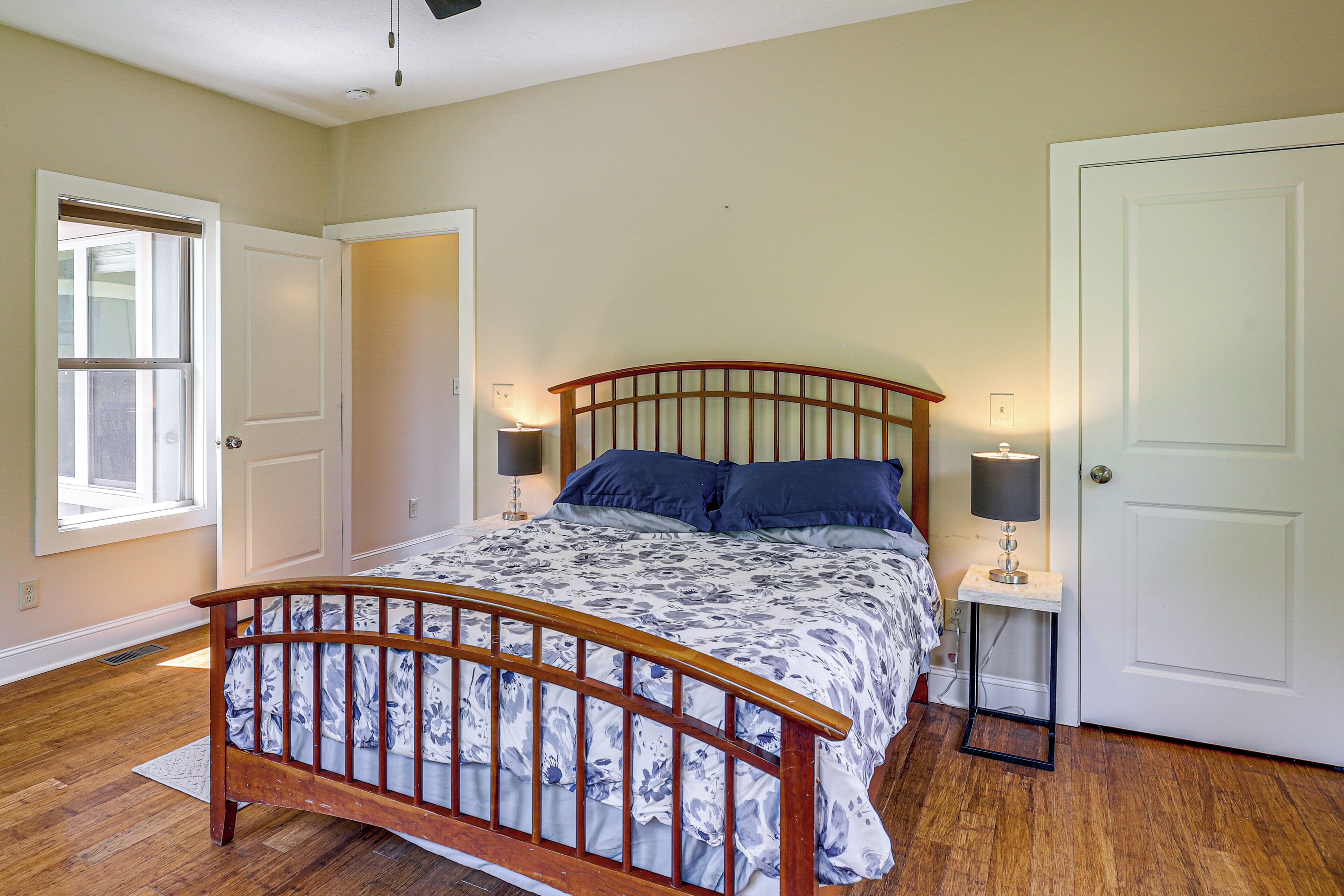 A bedroom with a wooden bed, two bedside tables with lamps, a window, and a door.