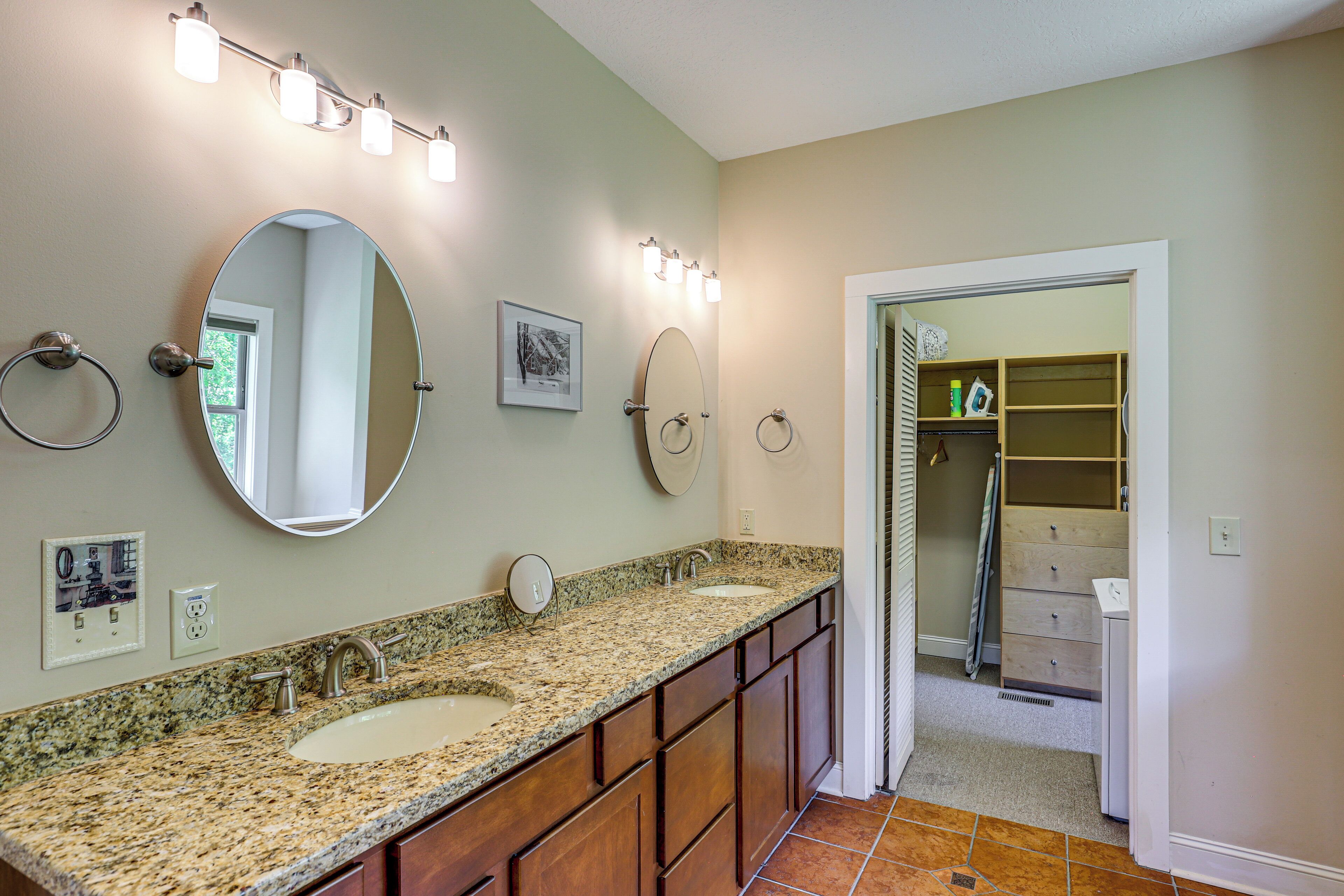 A bathroom with a granite countertop, two sinks, a large mirror, and a walk-in closet.