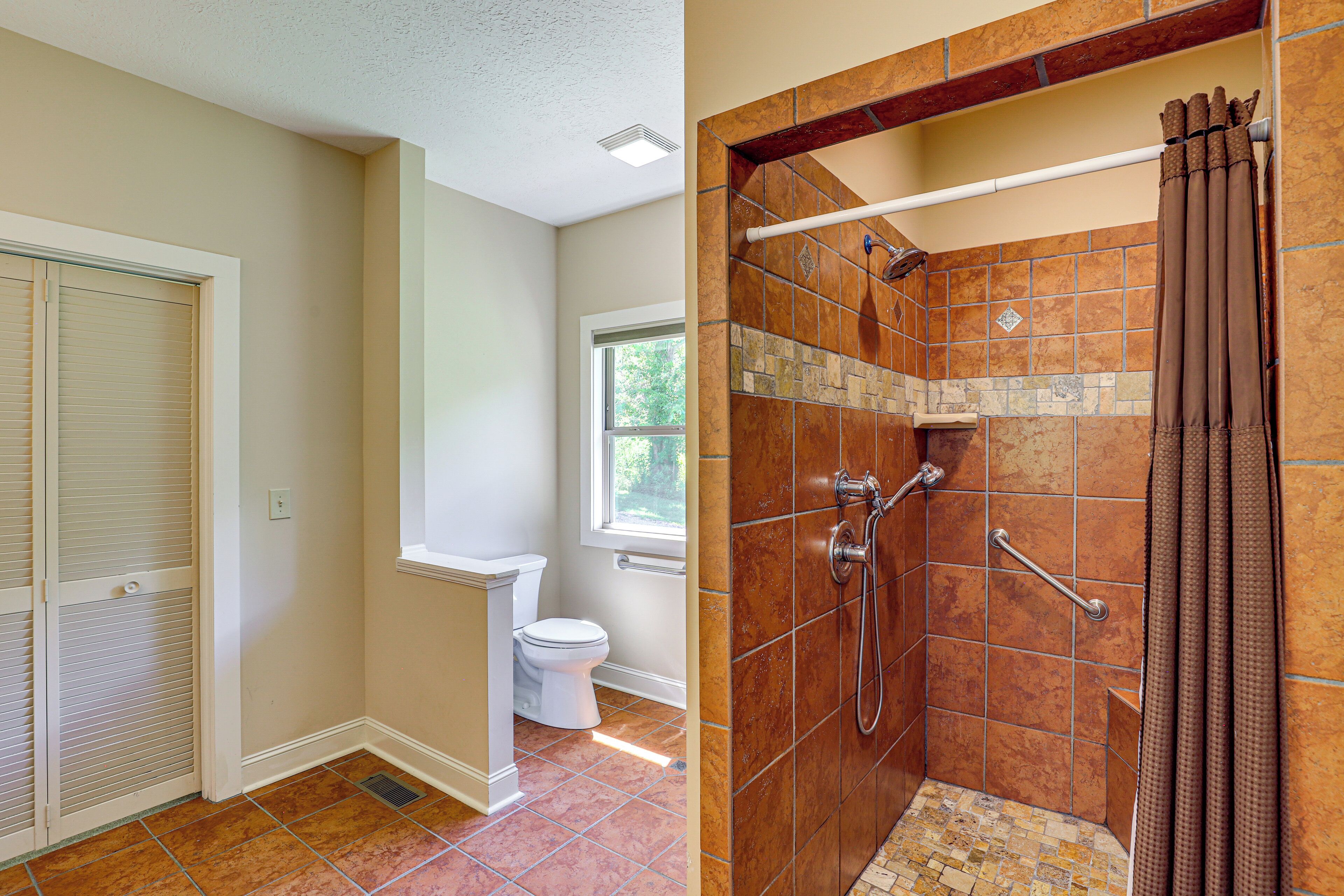 A bathroom with a toilet, shower, and a window.