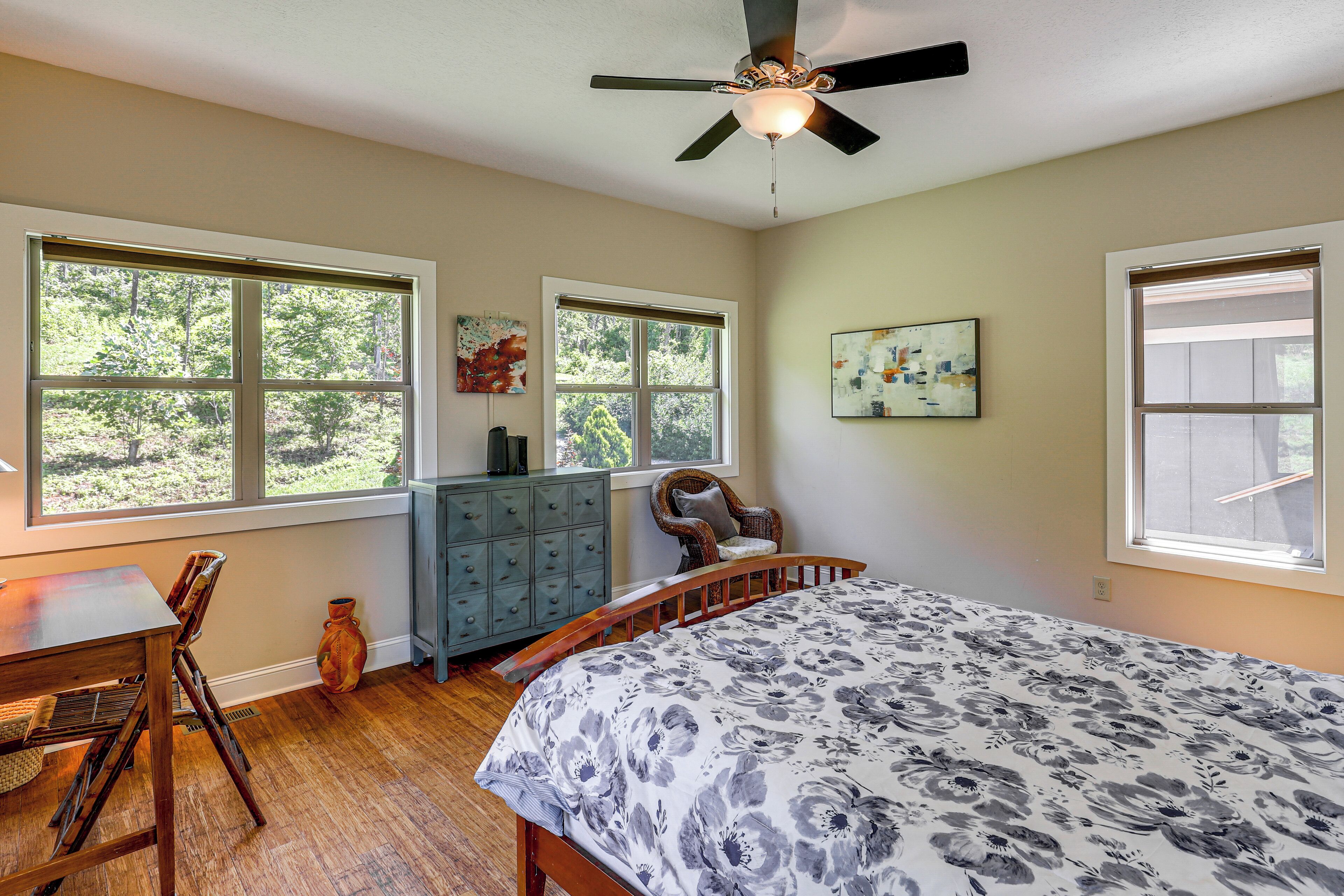A bedroom with a bed, a desk, a chair, a dresser, and two windows.