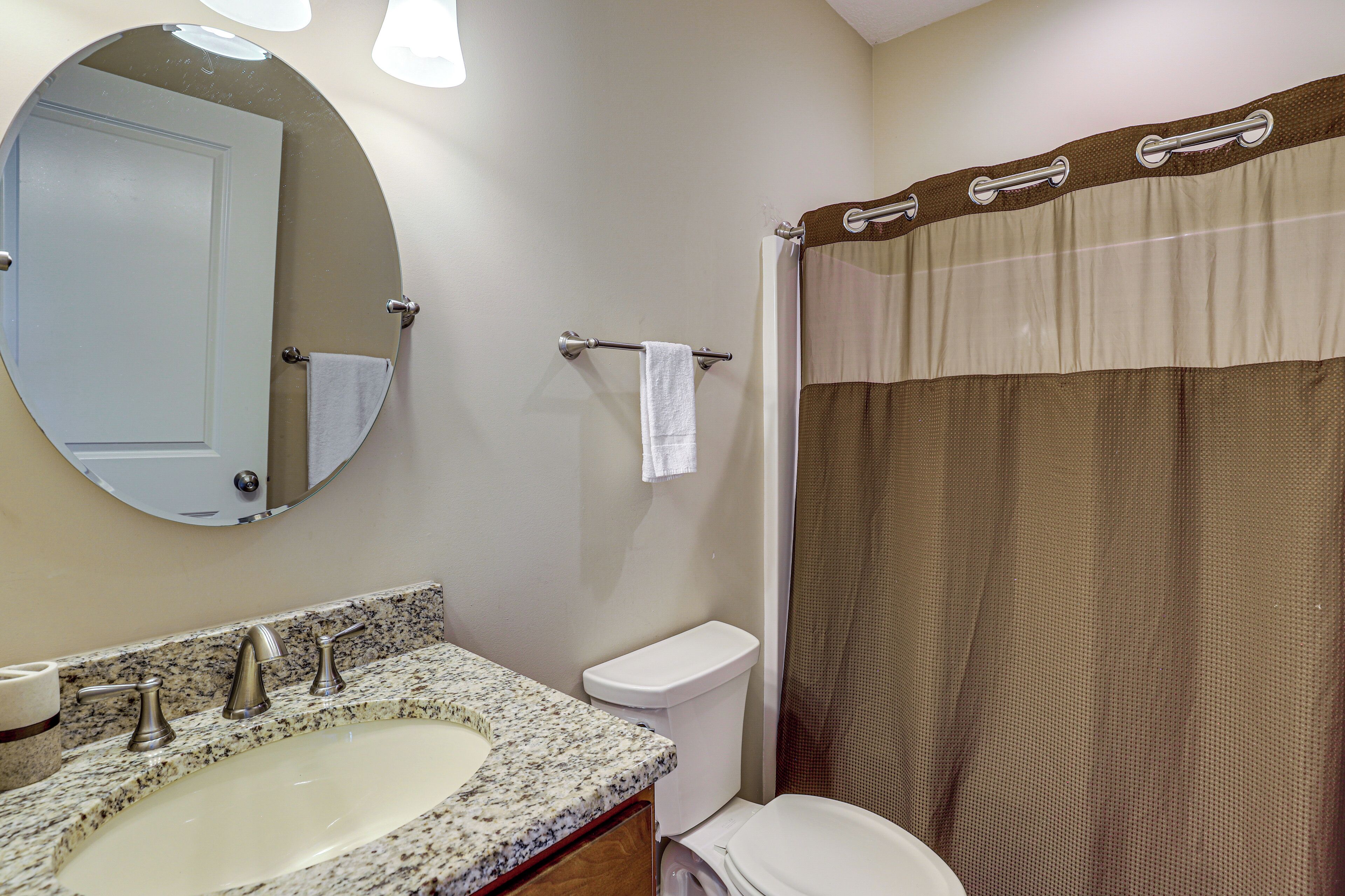 A bathroom with a sink, mirror, toilet, and shower curtain.