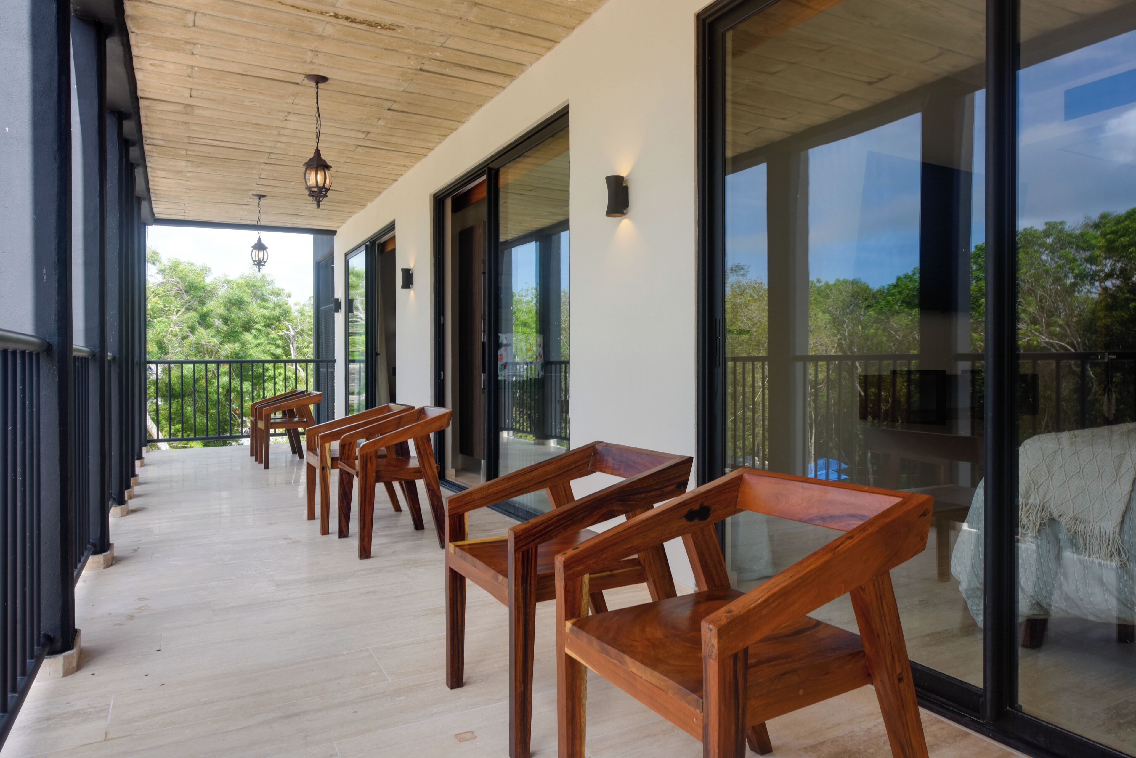 A covered outdoor seating area with wooden furniture and large glass doors leading to a balcony.