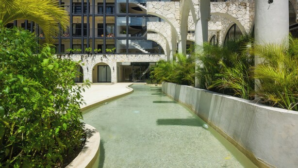 A modern building with multiple balconies, a central courtyard with a water feature, and surrounding greenery. - Resort Living in Tulum! Walkable Downtown Condo (Tulum)
