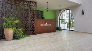A reception area with a wooden reception desk, potted plants, a green wall, and a large arched window. - Resort Living in Tulum! Walkable Downtown Condo (Tulum)