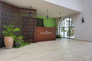 A reception area with a wooden reception desk, potted plants, a green wall, and a large arched window. - Resort Living in Tulum! Walkable Downtown Condo (Tulum)