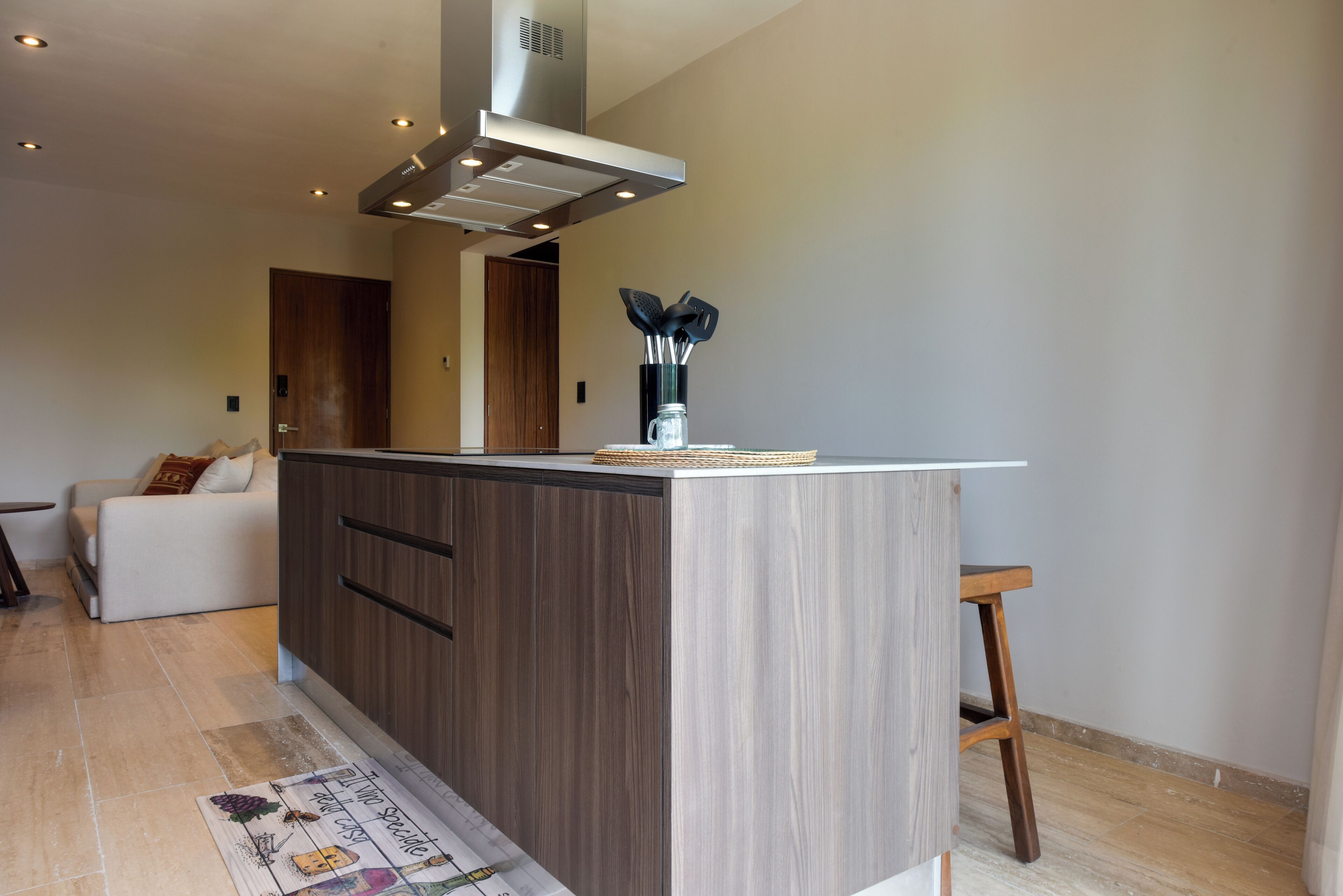 A modern kitchen with a central island, wooden cabinets, a stainless steel range hood, and a vase with utensils.