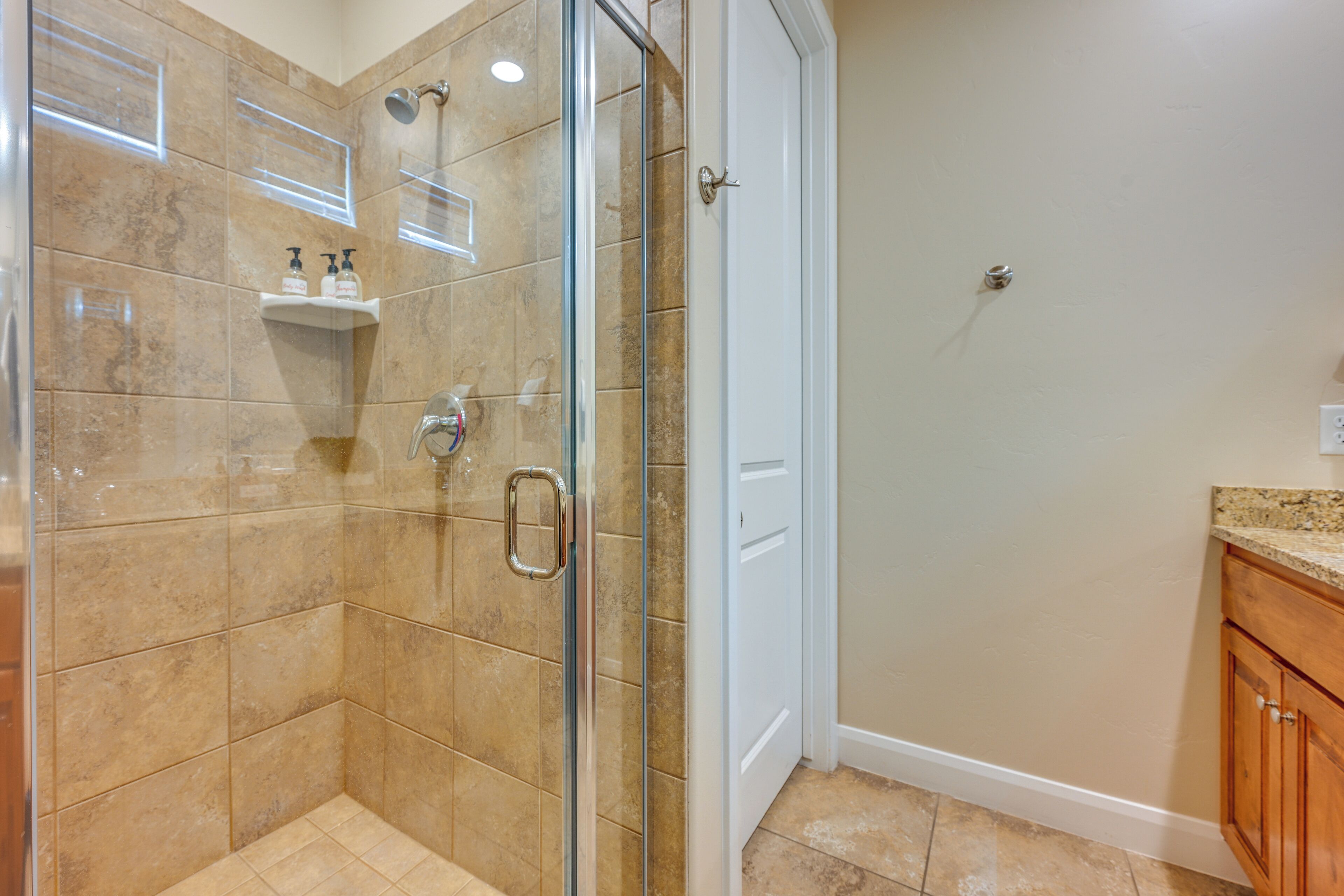 Un bagno con box doccia in vetro, piastrelle color crema, una porta bianca e un lavabo su un ripiano.