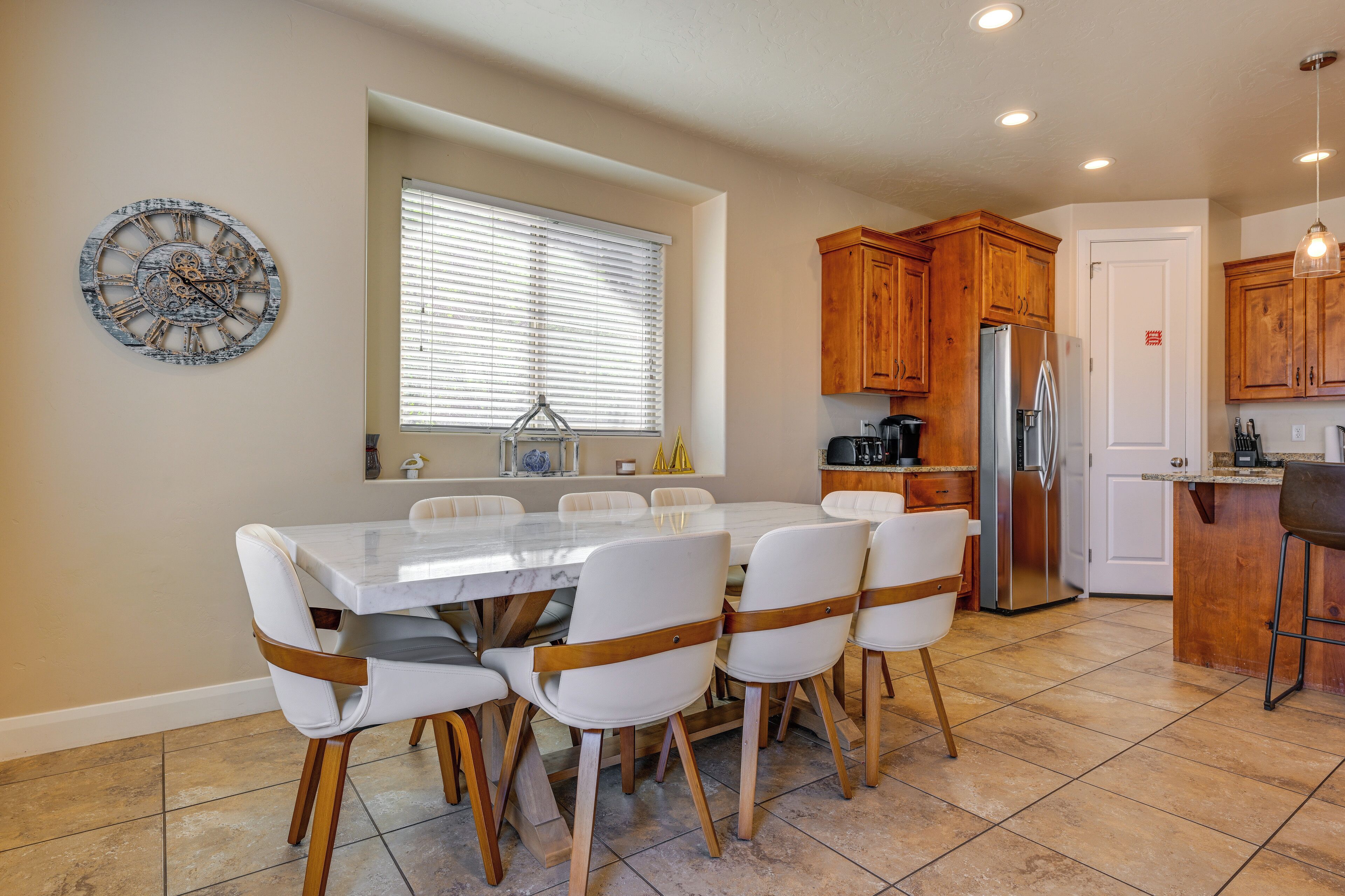 A dining area with a marble table and white chairs, a kitchen with wooden cabinets and stainless steel appliances, and a decorative clock on the wall.