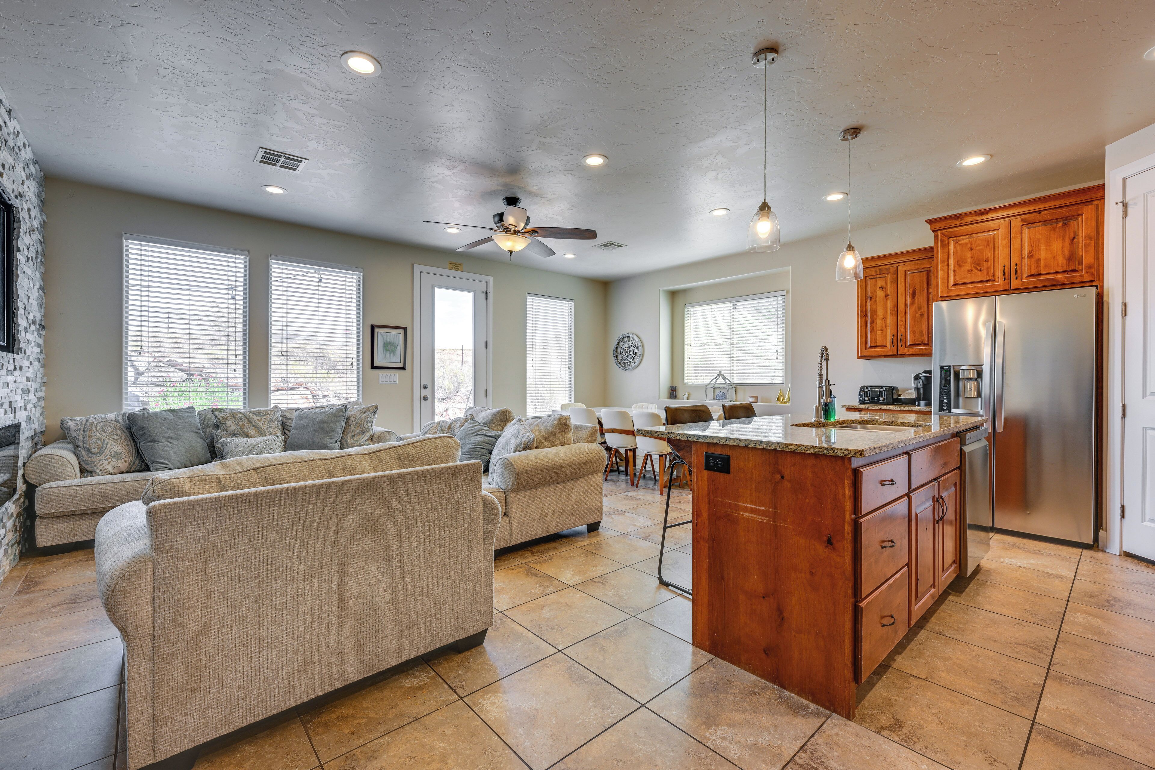 A spacious living area with a large sofa, a dining table, and a kitchen with wooden cabinets and a stainless steel refrigerator.