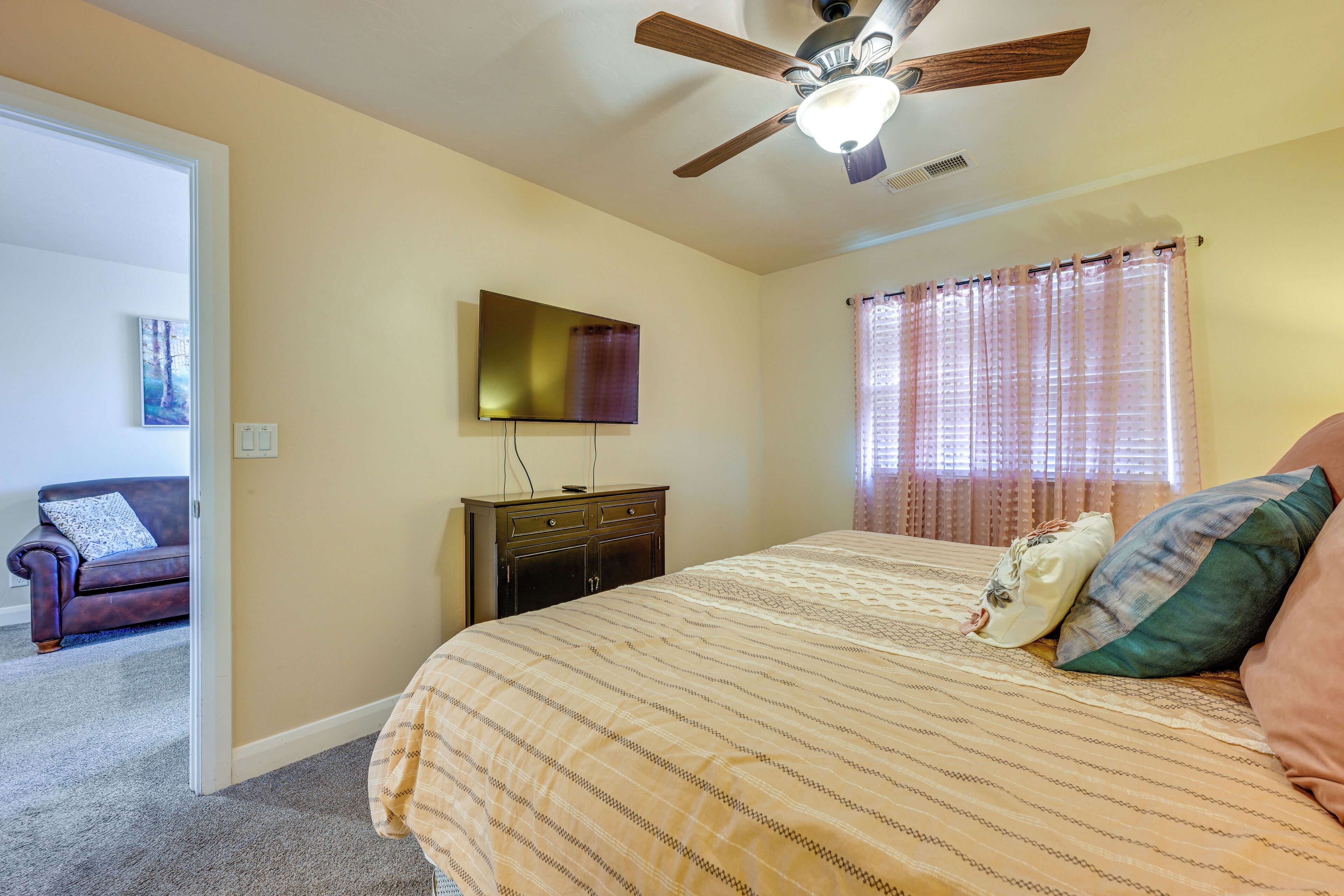 Une chambre à coucher comprenant un lit, un ventilateur de plafond, une commode, un téléviseur et une fenêtre avec des rideaux.