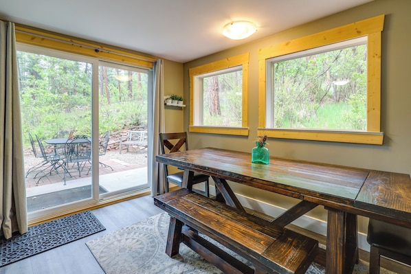 A wooden table with benches, a sliding glass door leading to an outdoor area, and a small shelf with plants. - Linger Longer Mtn-view San Isabel Forest Haven (Beulah)