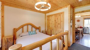 Una habitación con estructura de madera, una cama, una puerta de madera y un comedor con una mesa y sillas.