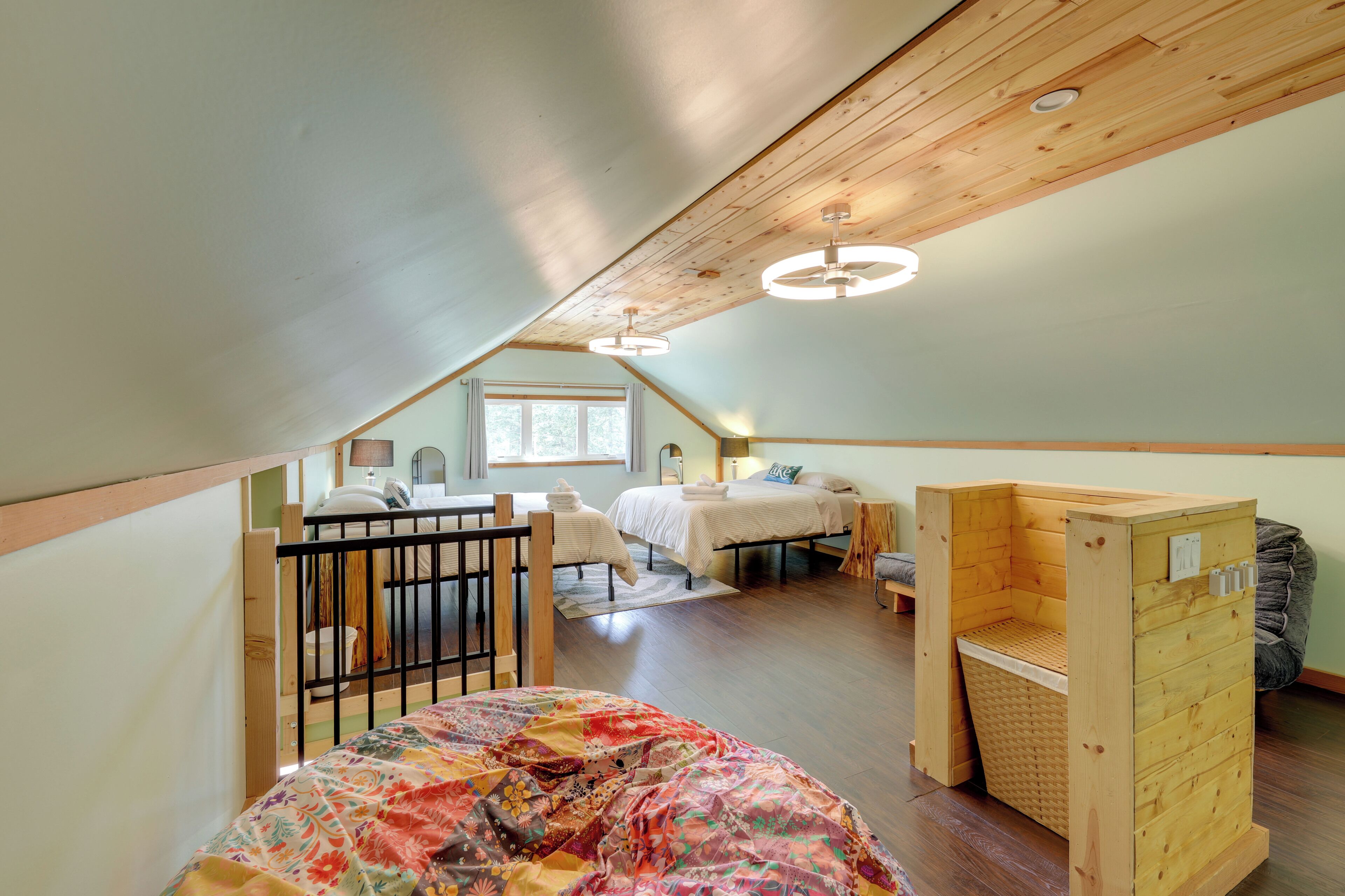 A loft-style bedroom with a wooden ceiling, two beds, a small seating area, and a wooden bench.