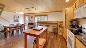 Un interior de madera con una mesa de comedor, sillas, una cocina con electrodomésticos y un ventanal.