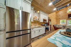A modern kitchen with stainless steel appliances, wooden cabinetry, and a dining area with a table and chairs. - Scenic Views! Dusk-to-dawn Barndominium (Hermitage)