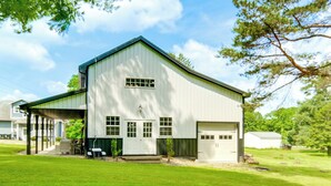 Ein weißes, barn-ähnliches Gebäude mit überdachter Veranda, einer Garage und einem gepflegten Rasen.