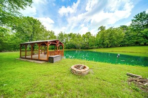 A wooden gazebo with a deck, a fire pit, and a pond in a grassy area. - Scenic Views! Dusk-to-dawn Barndominium (Hermitage)