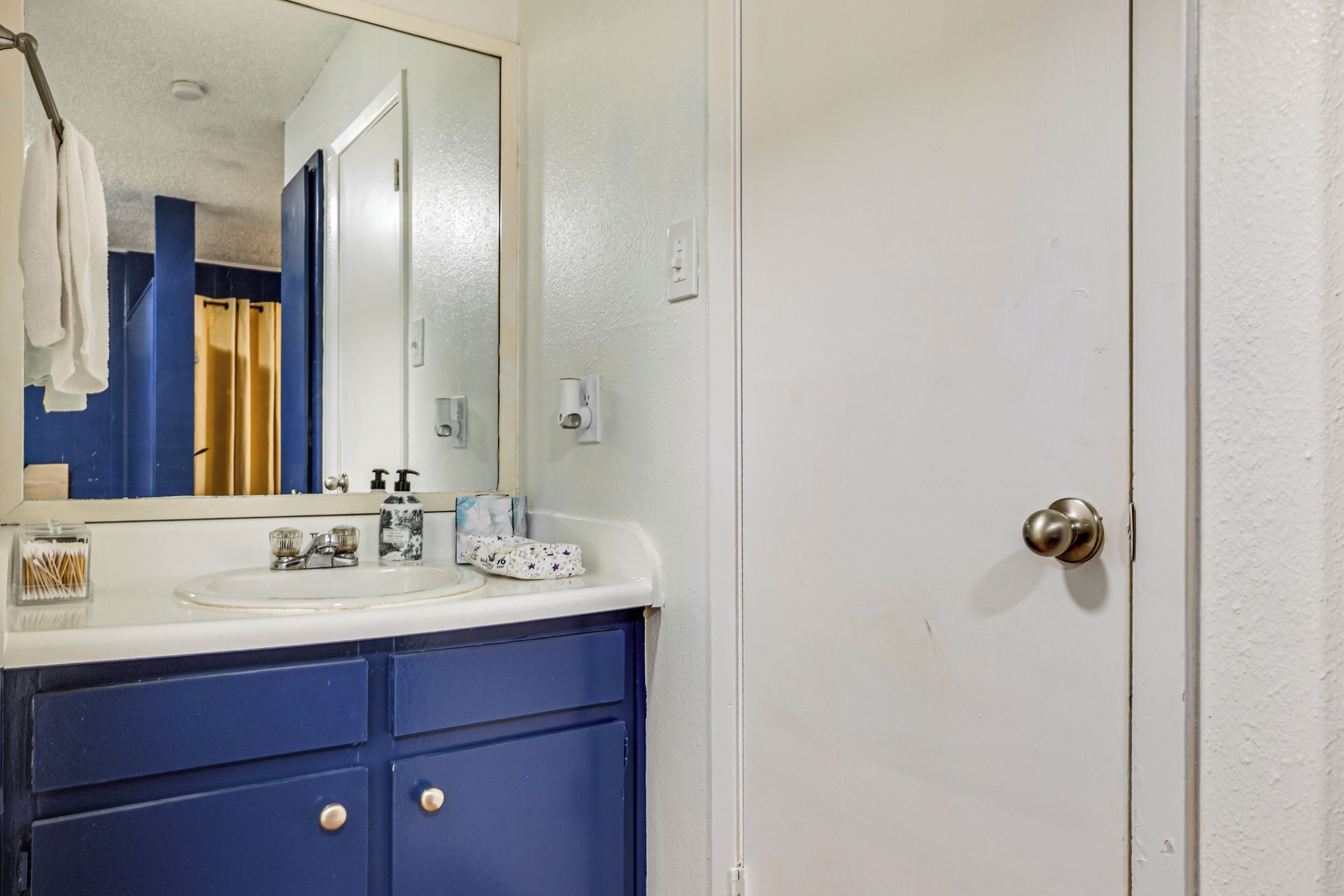 A bathroom with a white sink, blue vanity, and a mirror.