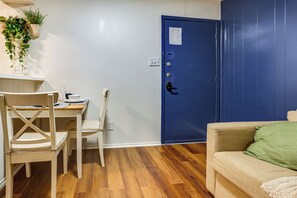Ein Zimmer mit Holzboden, einer blauen Tür, einem beigen Sofa und einem Esstisch mit Stühlen.