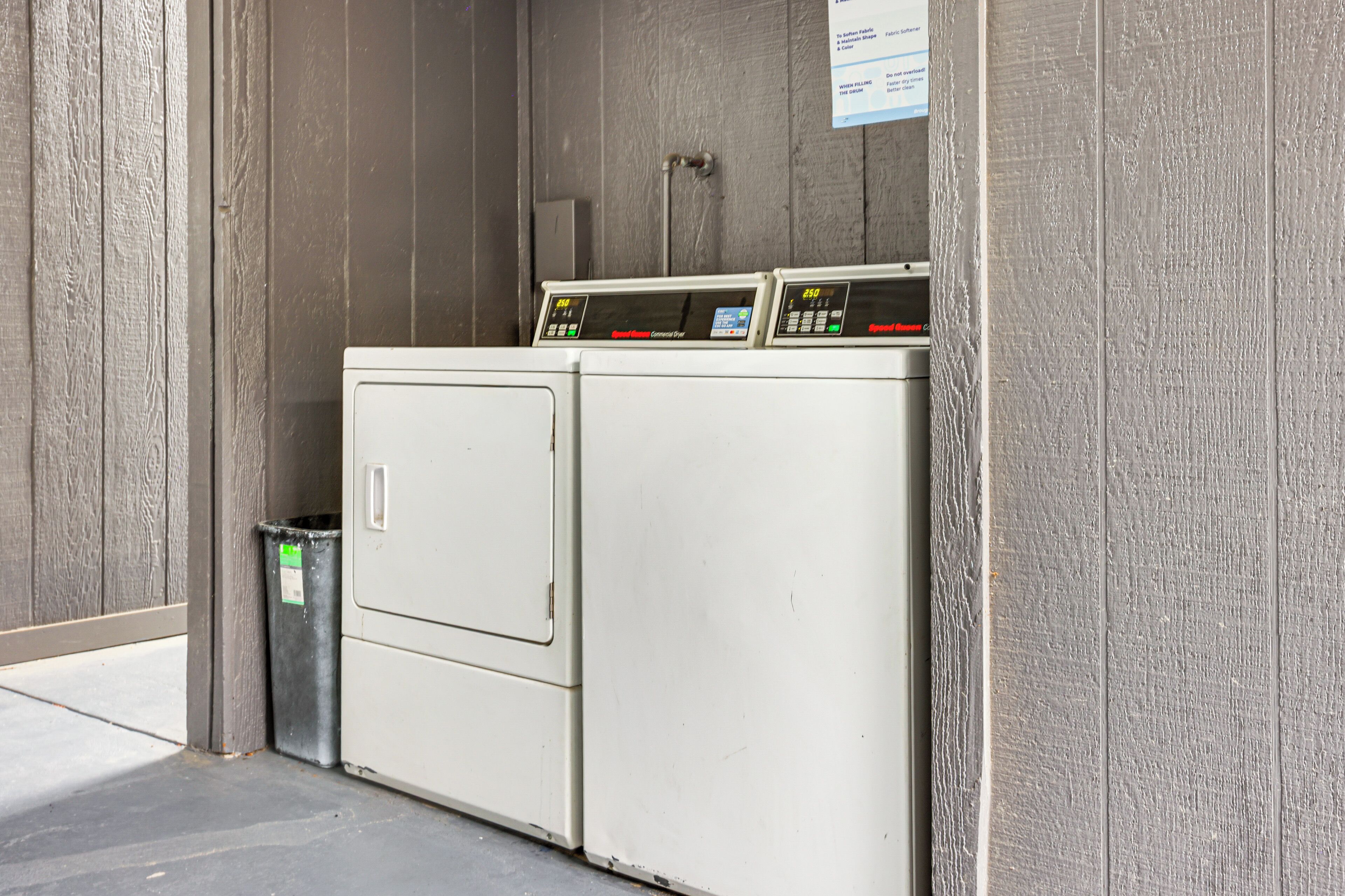 A laundry facility with two washing machines and a trash bin.