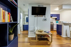 A room with a bookshelf, a table with books and a bowl, a television mounted on the wall, and a kitchen area with cabinets and appliances. - 1 Mi to UT & Med Centers! Updated Austin Studio (Austin)
