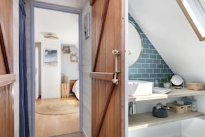 Ein Zimmer mit Holztür, Deckenventilator, Bett, kleinem Teppich und einem Regal mit diversen Gegenständen.