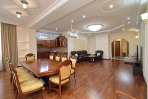 A spacious dining area with a large wooden table and chairs, a kitchen in the background, and a living area with sofas and a TV. - Apartment by Luxe Group AB917 (Yerevan)