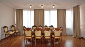 Een eetkamer met een houten tafel en stoelen, grote ramen met gordijnen en een plafond met inbouwverlichting.