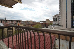 A view from a balcony with a red roof, overlooking a cityscape with various buildings, including a tall modern structure and older brick buildings. - Apartment by Luxe Group AB917 (Yerevan)
