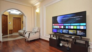 Een hotel lobby met een flatscreen televisie waarop verschillende zenders te zien zijn, een bank, houten vloeren en een deur die naar een andere kamer leidt.