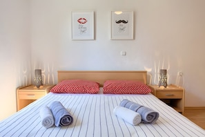 Quarto de hotel com cama, duas almofadas, duas mesas de cabeceira e duas luminárias fixadas na parede.