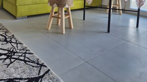 A bright living room with a green sofa, a small wooden stool, a table with a lace tablecloth, and a painting on the wall. - Mokshouse – Bright, Comfortable Apartment near City Center and Beach (Kavala)